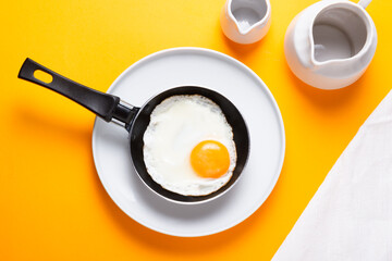 Scrambled, frying  eggs from one egg in a small pan on yellow background
