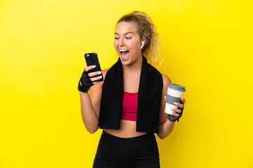 Sport woman with towel isolated on yellow background holding coffee to take away and a mobile