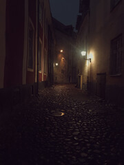 A dark street in the city with a glowing lantern, a rocky road
