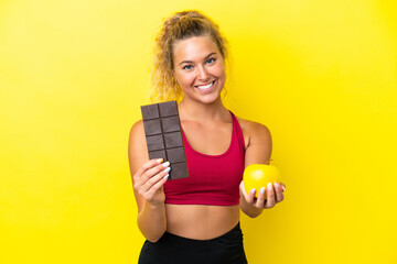 Girl with curly hair isolated on yellow background taking a chocolate tablet in one hand and an...