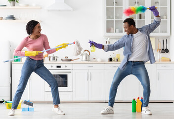 Funny african-american lovers fighting with cleaning tools