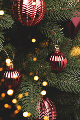 Closeup of fir tree with New Year decorations. Trendy red Christmas ornaments with golden bokeh.