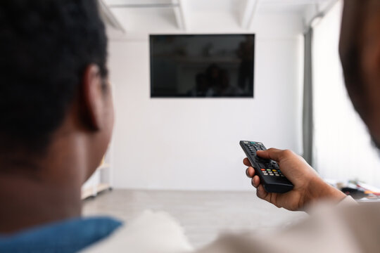 Black couple watching TV with mockup and using remote controller