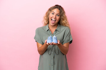 Girl with curly hair isolated on pink background pregnant and holding baby booties