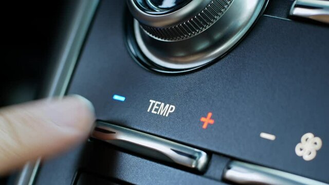 A woman lowers the temperature of the car's climate control by pushing a close-up chrome button