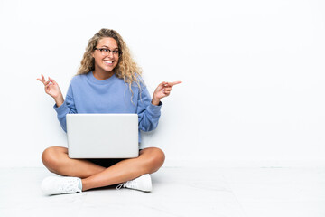 Naklejka premium Girl with curly hair with a laptop sitting on the floor pointing finger to the laterals and happy