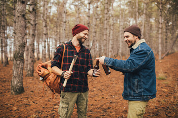 Two millennial man hiking and drinking beer in a forest, laughing and having fun.