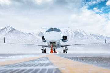 Front view of the white luxury corporate business jet on the winter airport apron on the background...