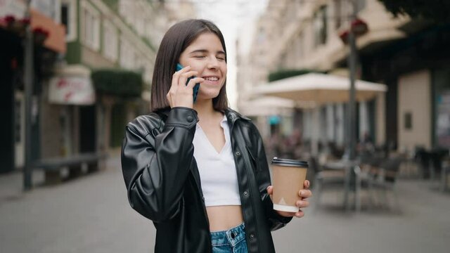 Young hispanic woman talking on the smartphone drinking coffee at street