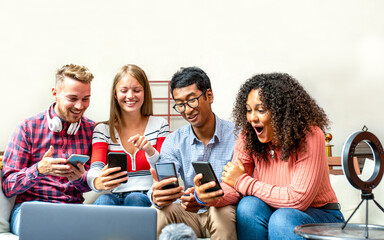 group of young contents creators looking at smartphones their achievement on line, four people bloggers working in studio for business, youth teamwork sharing on mobile app and laptop creative content