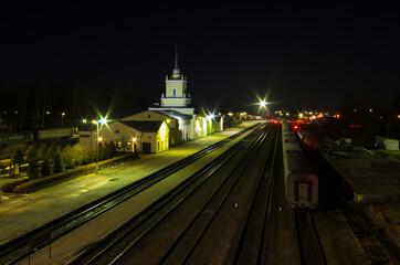 Fototapeta na wymiar Night landscape of a railway hub with a station building and rays of lanterns (Pskov region, Russia)