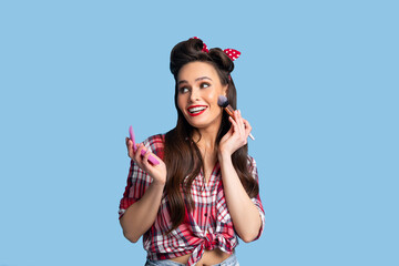 Bright makeup. Sexy young pinup lady in retro outfit putting on decorative cosmetics with brush...