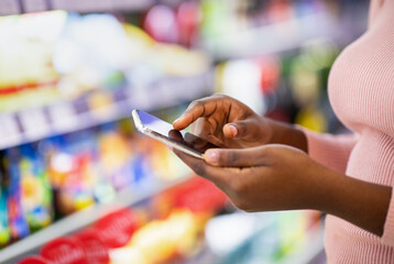 Cropped view of young black woman checking grocery list app on cellphone at supermarket, copy space