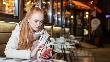 beautiful, long-haired, red-haired girl, with a mobile phone, at a cafe, in the evening