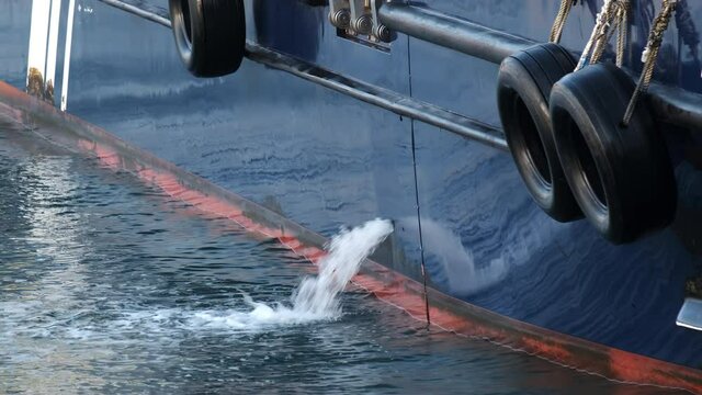 Bilge water discharging from industrial ship side into blue ocean.