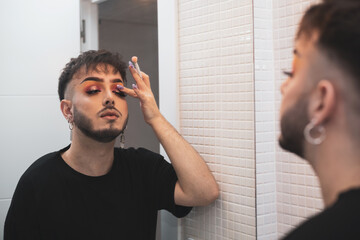 a young gay man puts on makeup in the bathroom of his house to go outside.