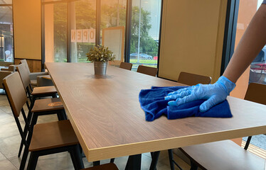 Close-up image of female hands wear blue glove cleaning table in the shop. Janitor's Hand Cleaning Wooden Desk With Soft Cloth,