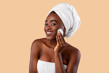 Portrait of excited black woman cleaning skin by cotton pad