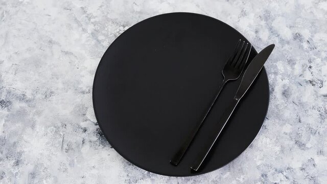 black dining plate with fork and knife on gray background with minimalist composition, dieting vs intuitive eating