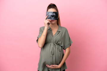 Young woman isolated on pink background pregnant and holding an ultrasound