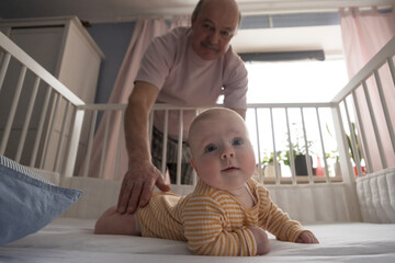 Cheerful senior grandfather playing with grandson at the bedroom