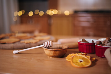 Home bakery, cooking traditional festive sweets. Preparing for making gingerbread dough on wooden table. New Year celebration traditions. Honey and dried orange wedges. Christmas mood