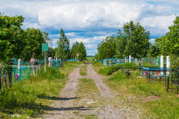 Perspective view of a track between graves in the Zaykovskoye Cemetery in sunny summer day, Kurgan, Russia
