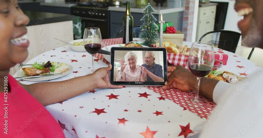 Canvas Prints Smiling african american couple using tablet for christmas video call with happy couple on screen