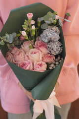 Fashionable bouquet of flowers in green paper tied with a pink ribbon in female hands. Bouquet of roses, decorative carnations, eucalyptus.