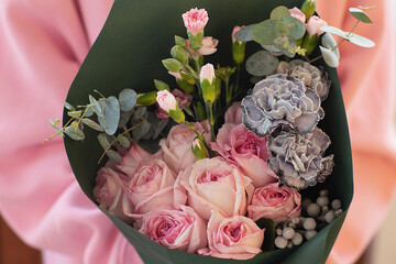 Fashionable bouquet of flowers in green paper tied with a pink ribbon in female hands. Bouquet of roses, decorative carnations, eucalyptus.