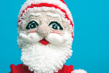 the face of a knitted Santa Claus toy on a blue background close-up.