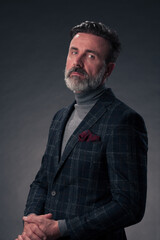 Portrait of a stylish elegant senior businessman with a beard and casual business clothes in photo studio isolated on dark background gesturing with hands