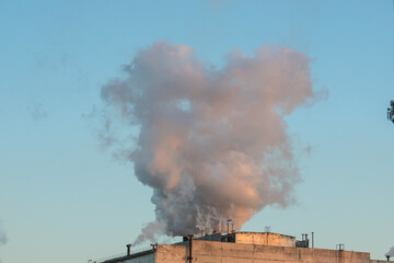 Brick chimney with white smoke over an industrial building