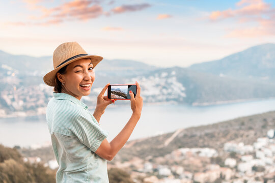 Tourist girl taking photos on smartphone of the scenic beach in resort town. Sightseeing and travel blogger concept