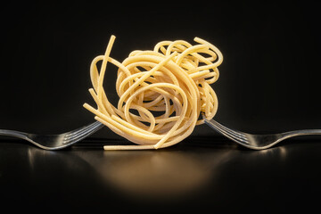 Creative still life photo of two forks with raw pasta on black background