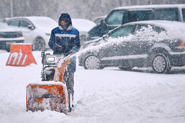 Man remove snow from parking lot with snow blower machine during snowfall. Worker blowing snow...