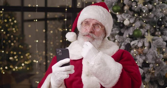 Brooding Santa reads the message on his smartphone, strokes his mustache and looks around, nodding his head with a negative decision, with the inability to satisfy a child's wish.