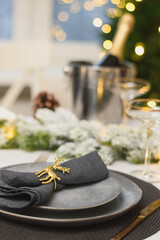 Christmas elegant table setting decorated gold garland, gray plate with napkin ring, Family holiday dinner ar home or night New Year party. Vertical format. Close up.