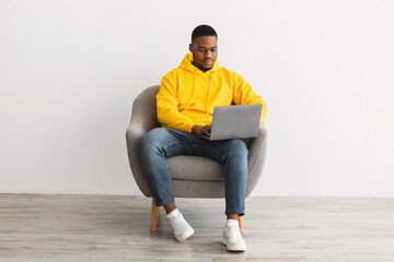 Black Guy Using Laptop Working Online Sitting On Gray Background