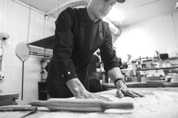 Professional chef cooking in the kitchen restaurant at the hotel, preparing dinner. A cook in an apron makes a pizza. man rolls out pizza dough