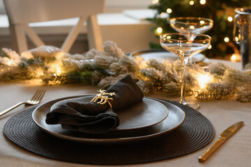 Christmas elegant table setting decorated gold garland, gray plate with napkin ring. Family holiday dinner ar home. Close up.