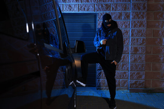 Man in balaclava with gun near van outdoors - Powered by Adobe