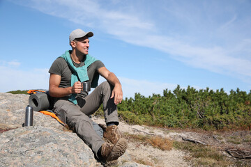 Tourist with hot drink, sleeping bag and mat on mountain peak