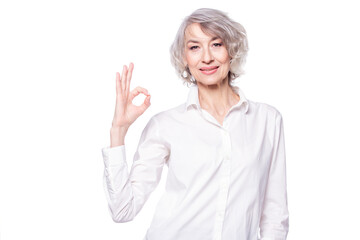 Portrait of a mature attractive woman wearing elegant shirt standing over isolated white background smiling with happy face doing okay sign