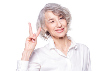Close up portrait of senior grey-haired woman wearing elegant shirt standing over isolated white background smiling with happy face winking at camera doing victory sign