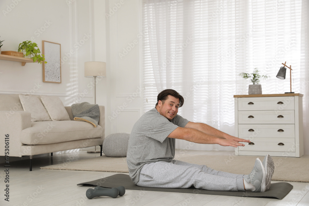 Sticker Overweight man stretching on mat at home, space for text