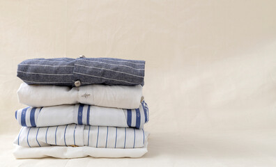 Stack of striped linen,cotton shirts on the beige organic linen fabric.Empty space