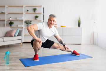 Morning routine. Mature man warming up and stretching, preparing for workout, training on mat in...
