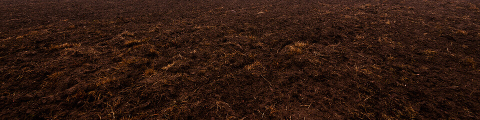 Plowed agricultural field, tractor tracks, soil texture close-up. Rural scene. Panoramic landscape. Farm and food industry, alternative energy and production, environmental conservation theme - obrazy, fototapety, plakaty