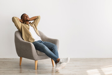 Happy African American Man Relaxing Sitting In Chair, Gray Background